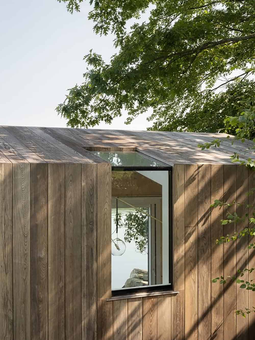 Weathered cedar cladding detail with clerestory window reflecting lake and interior pendant light