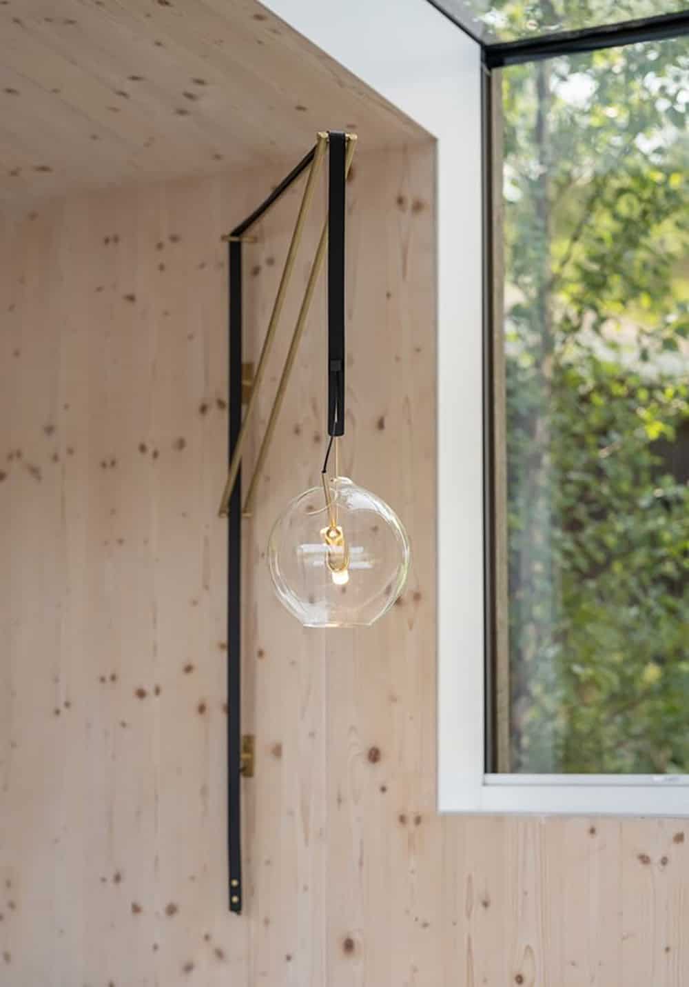 Brass and black wall-mounted pendant light against CLT wall panels beside a large window