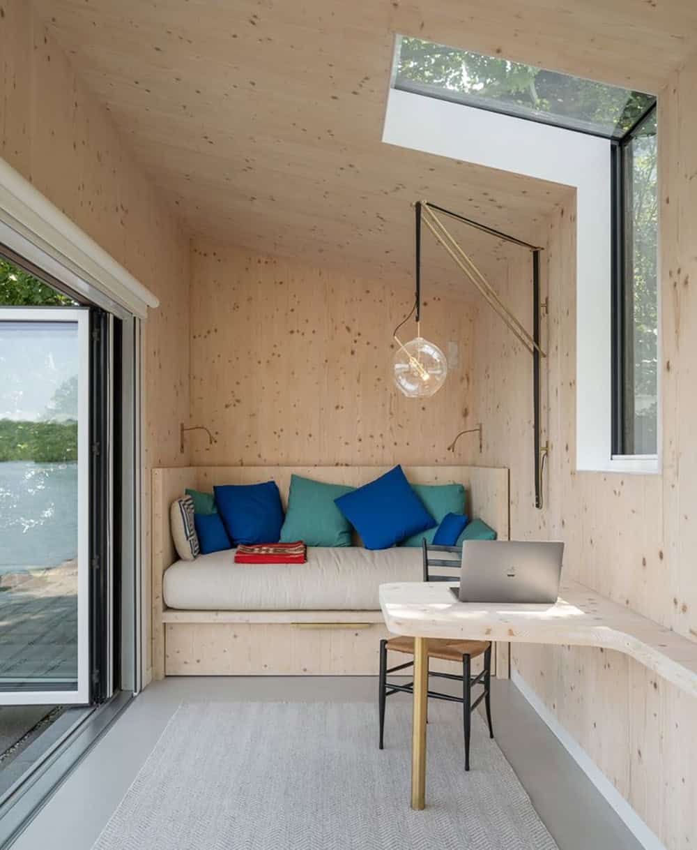 Interior of CLT lakeside studio with built-in daybed, skylight, brass pendant light, and fold-down desk