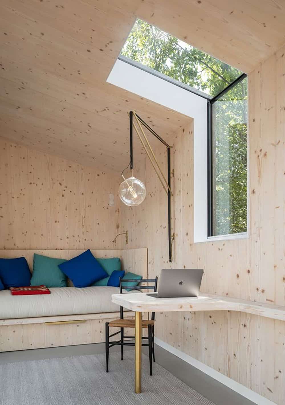 CLT studio interior with corner skylight, built-in bench seating, and fold-down CLT desk
