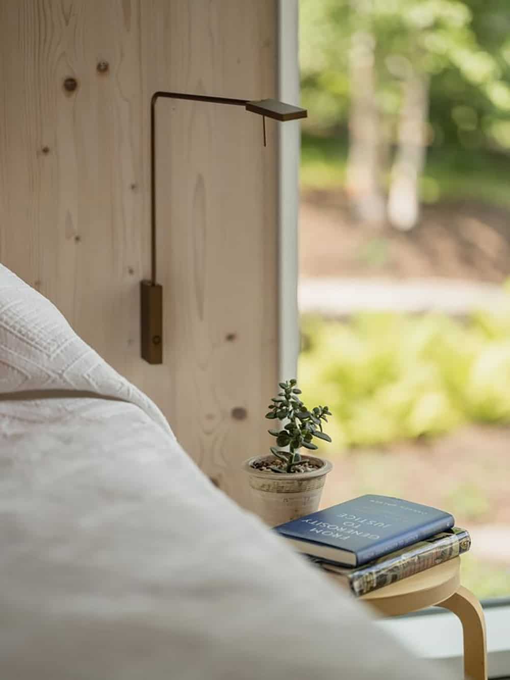 Bedside detail with brass reading lamp, succulent, and stacked books on a wood nightstand against a CLT wall