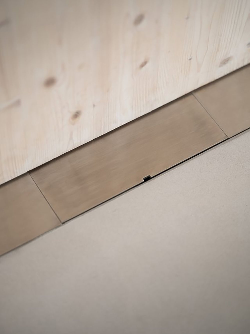 Brushed metal threshold strip at the base of a CLT wall meeting a concrete floor
