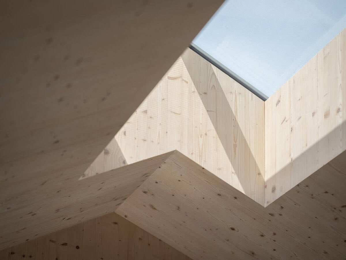 Geometric CLT skylight well with angled timber panels casting dramatic shadows