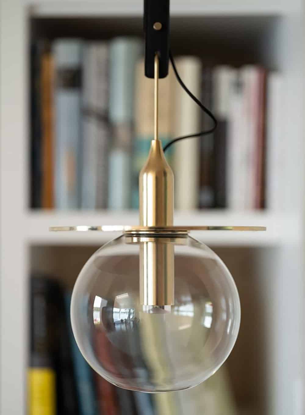 Close-up of a brass and glass globe pendant light hanging in front of built-in bookshelves