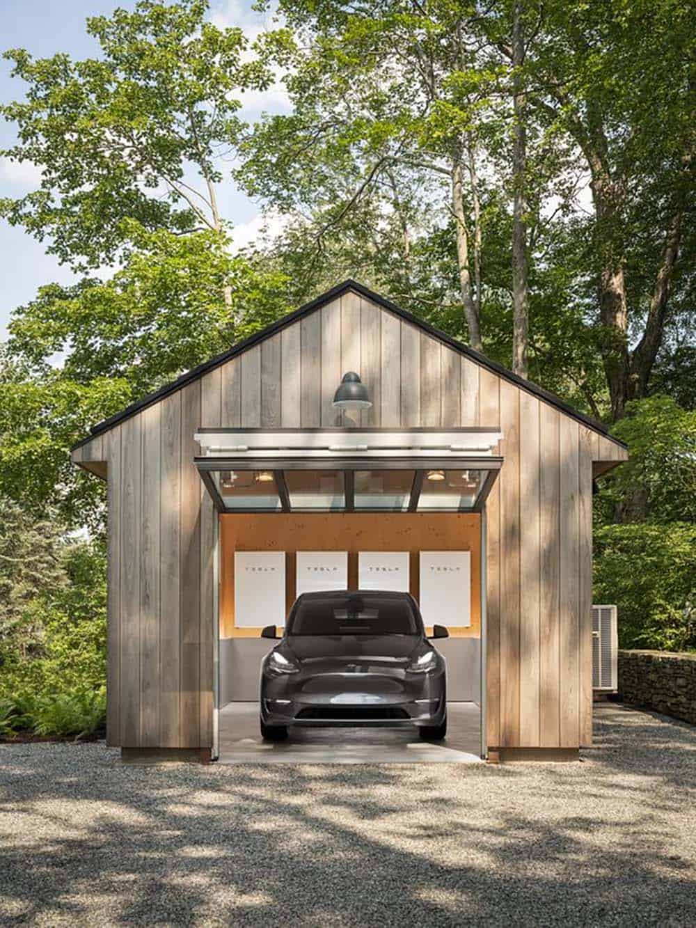 Cedar-clad prefab garage with glass garage door open to reveal a Tesla and Powerwall batteries