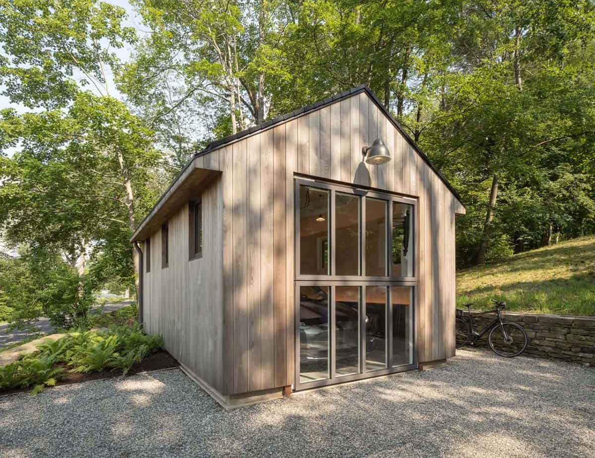 Weathered cedar studio outbuilding with large glass sliding doors on a gravel path