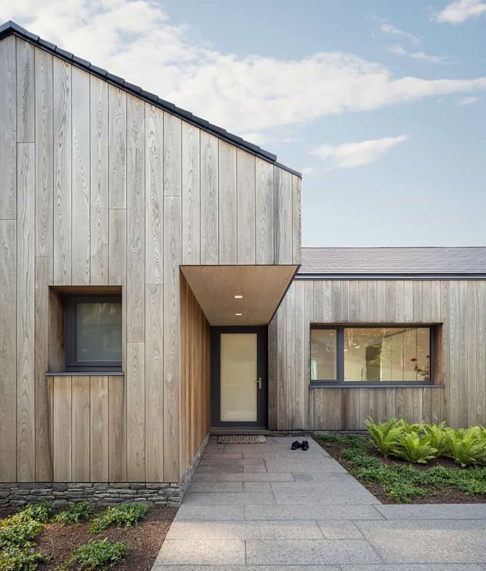 Front entry of prefab Connecticut lake house with cedar cladding, cantilevered canopy, and granite path