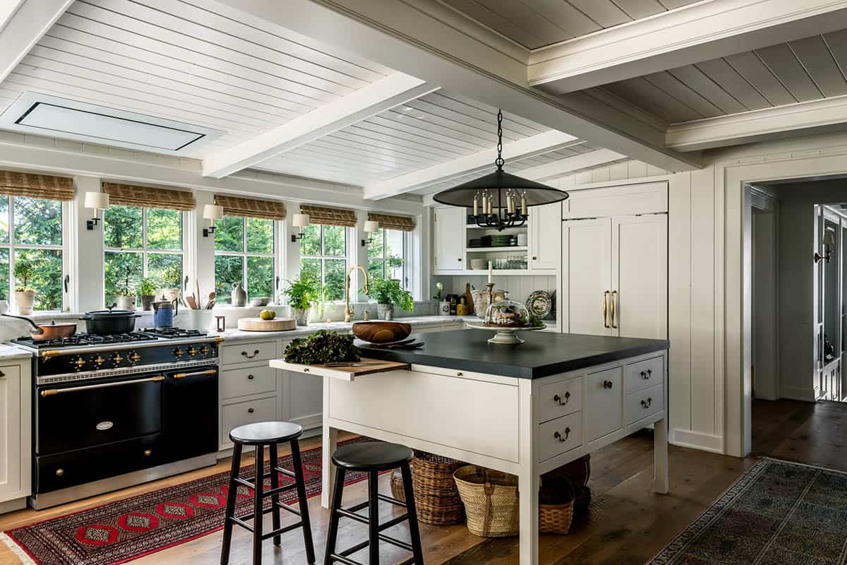 Open kitchen with black island, Lacanche range, pendant light, and woven shades