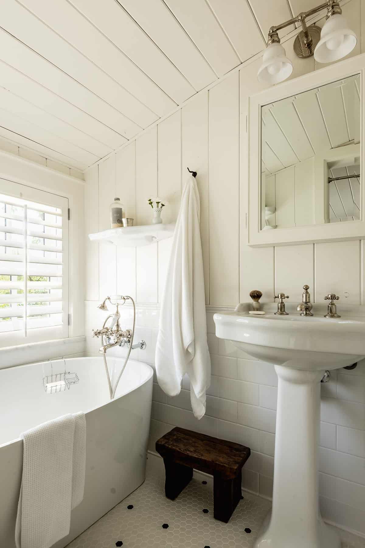 All-white bathroom with soaking tub, pedestal sink, subway tile, and hex floor