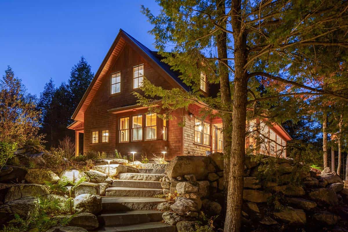Night view of cedar camp exterior with illuminated stone steps, boulder landscaping, and warm glowing windows