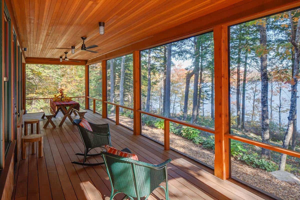Screened porch with wood ceiling, rocking chairs, picnic table, and sweeping forest and lake views