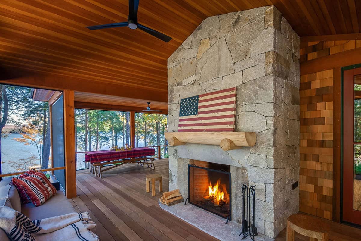 Covered porch with floor-to-ceiling granite fireplace, log mantel, American flag artwork, and wood-plank ceiling
