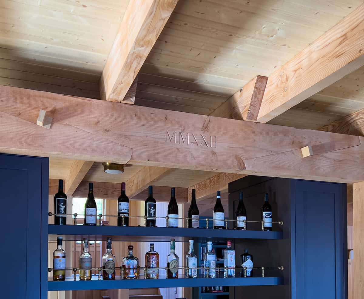 Detail of exposed timber beam engraved with MMXXII above a built-in bar with wine and spirits shelves