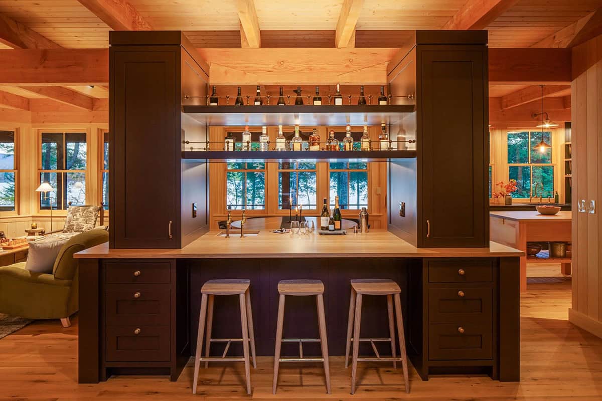 Built-in bar with dark cabinetry, mirrored back, brass fixtures, wood countertop, and three bar stools