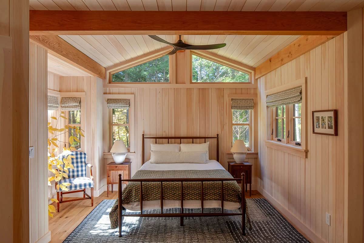 Bright bedroom with vaulted ceiling, iron bed frame, wood-paneled walls, and clerestory gable windows