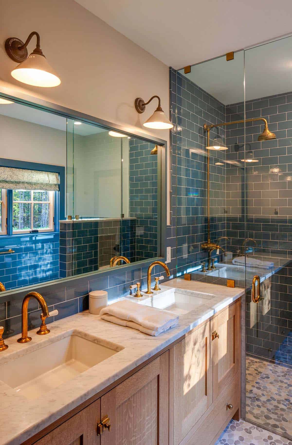 Primary bathroom with blue subway tile, double marble vanity, brass fixtures, and glass-enclosed shower