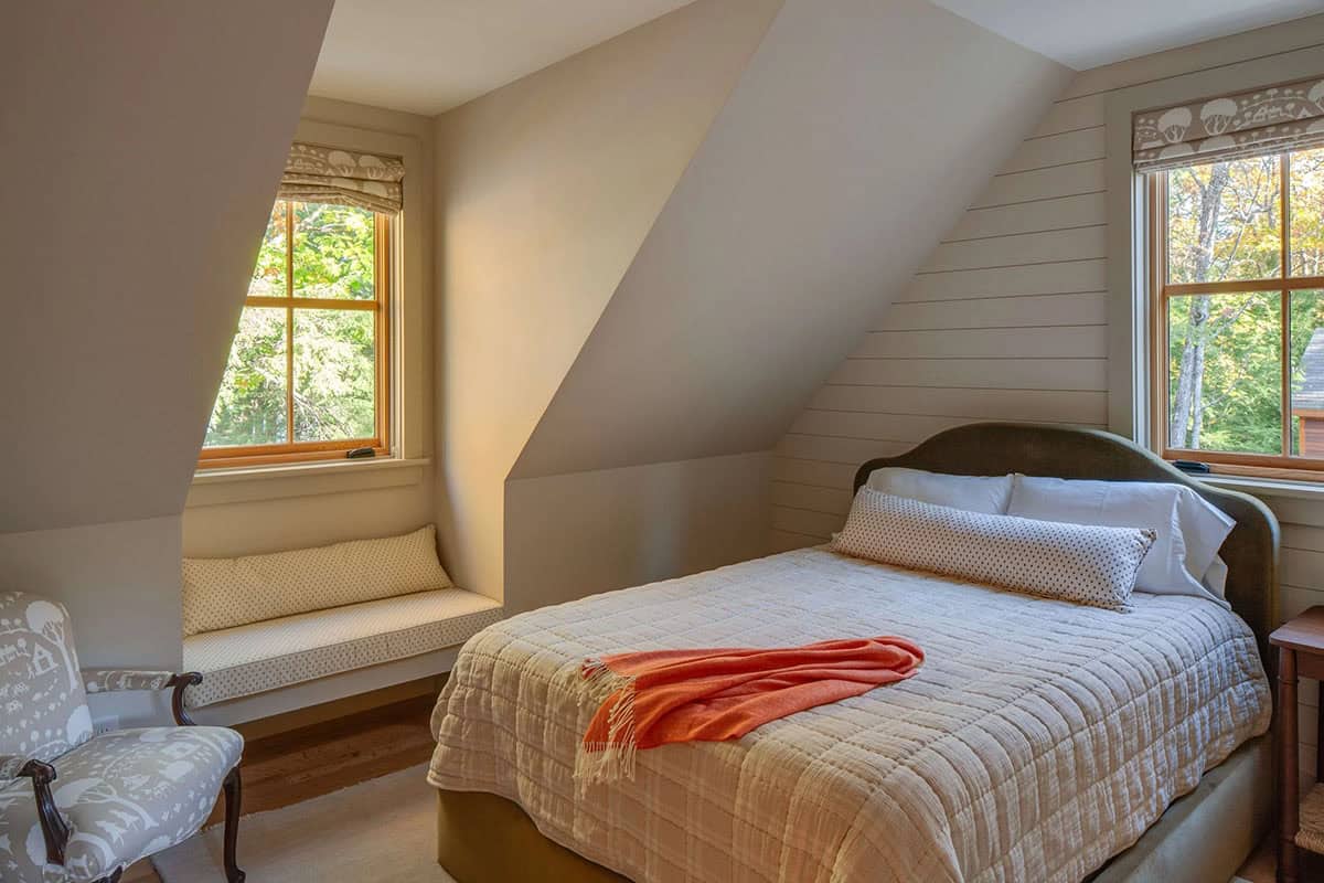 Cozy attic bedroom with sloped ceiling, built-in window seat, shiplap wall, and treetop views