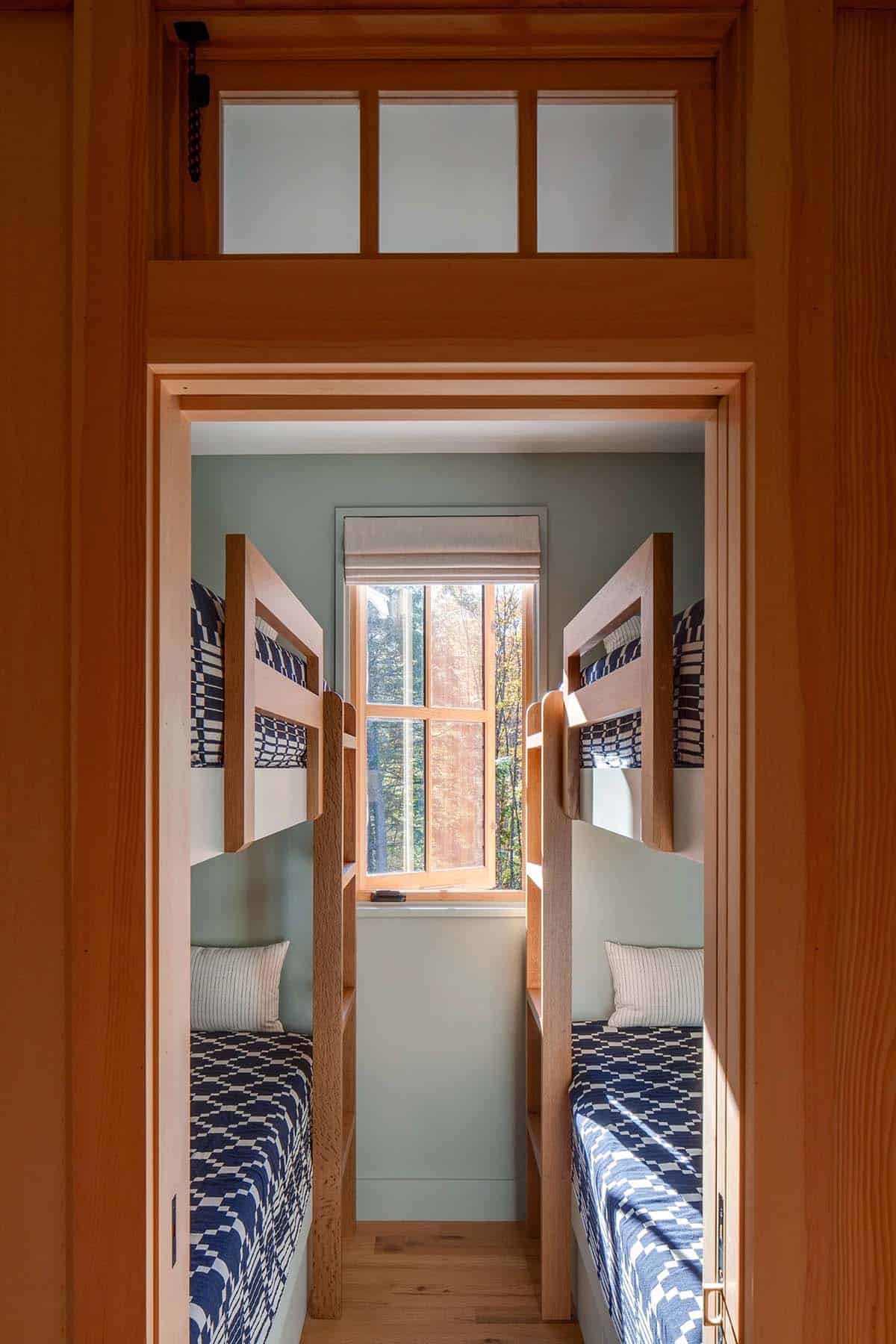 Compact bunk room with four maple bunk beds, sage green walls, and center window framing autumn foliage
