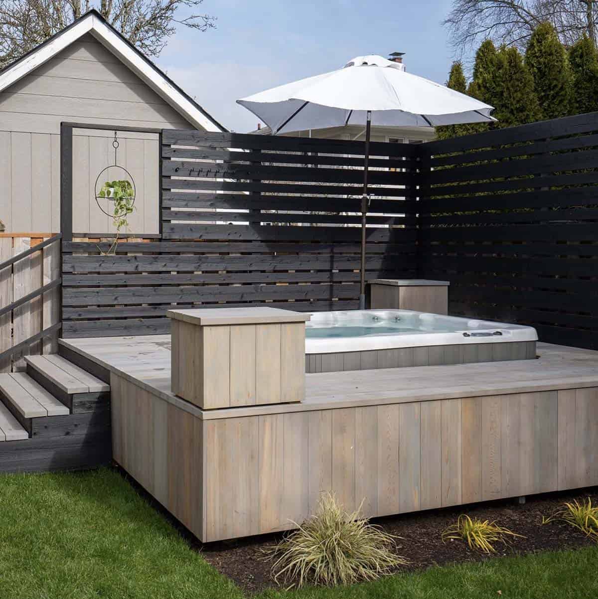 A raised hot tub deck with a black slatted privacy screen built into the same backyard corner in Portland, Oregon