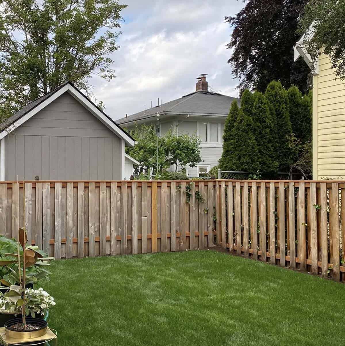 An empty grass backyard corner with a wood picket fence before a hot tub deck renovation in Portland, Oregon