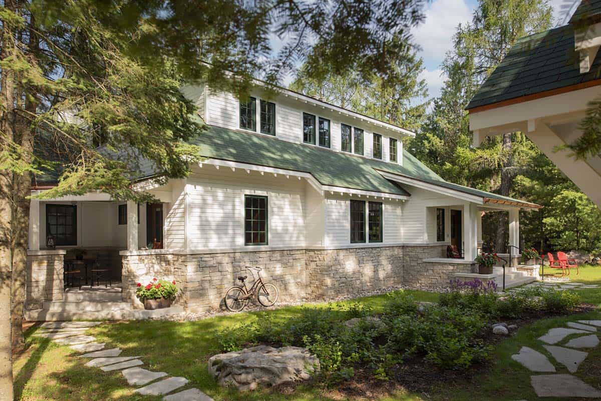 Side view of cabin exterior showing green roof, stone base, covered porch, and landscaped grounds