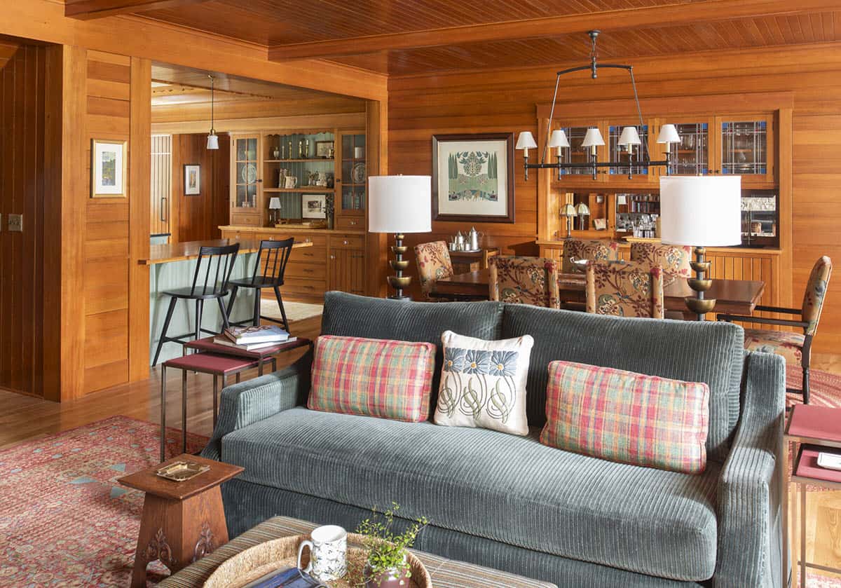 Open-plan living and dining area with cedar walls, gray corduroy sofa, and built-in hutch