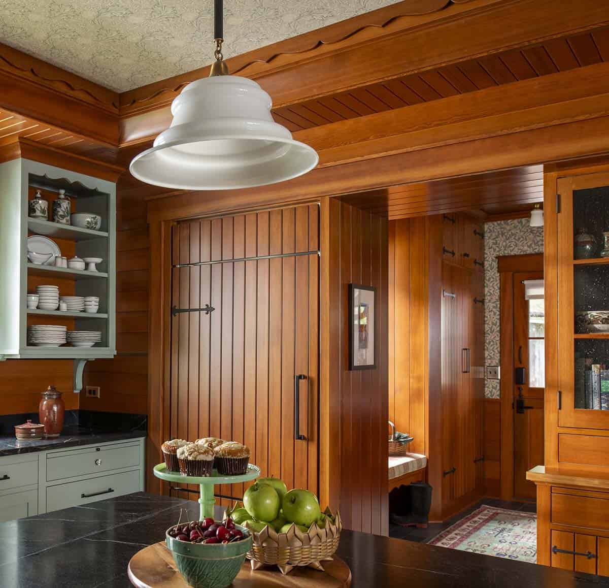 Kitchen detail showing wood-paneled refrigerator, white pendant light, and sage green cabinetry
