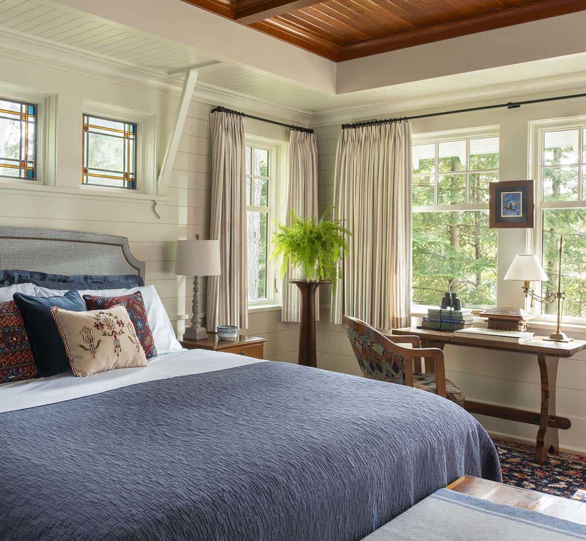 Bright primary bedroom with white shiplap walls, stained glass windows, and cedar ceiling detail