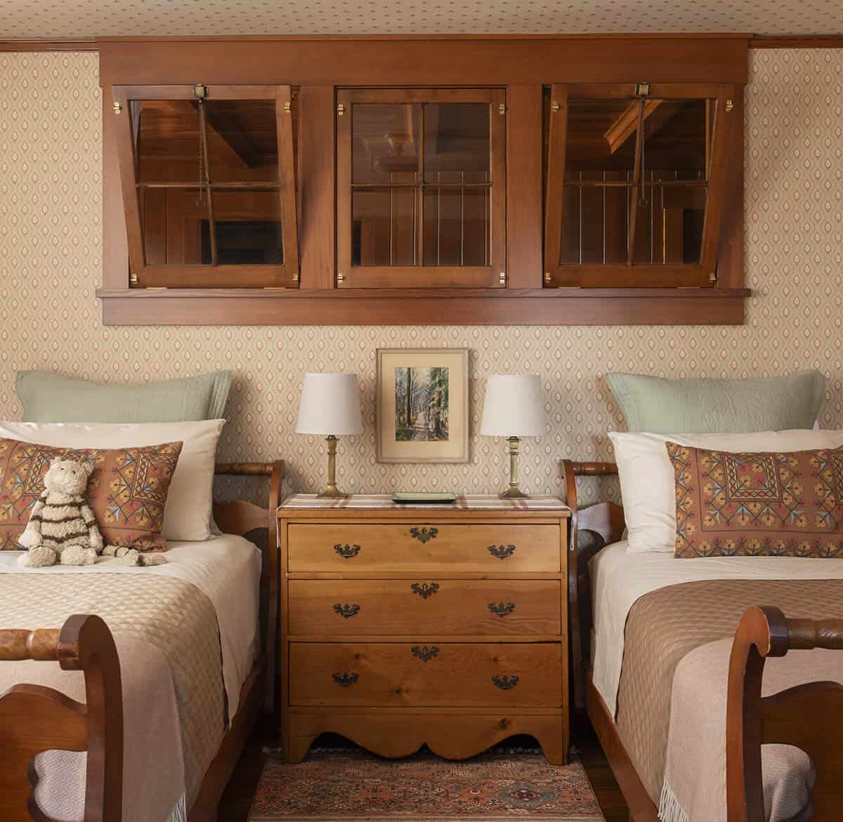 Twin bedroom with patterned wallpaper, matching sleigh beds, and overhead wood transom windows
