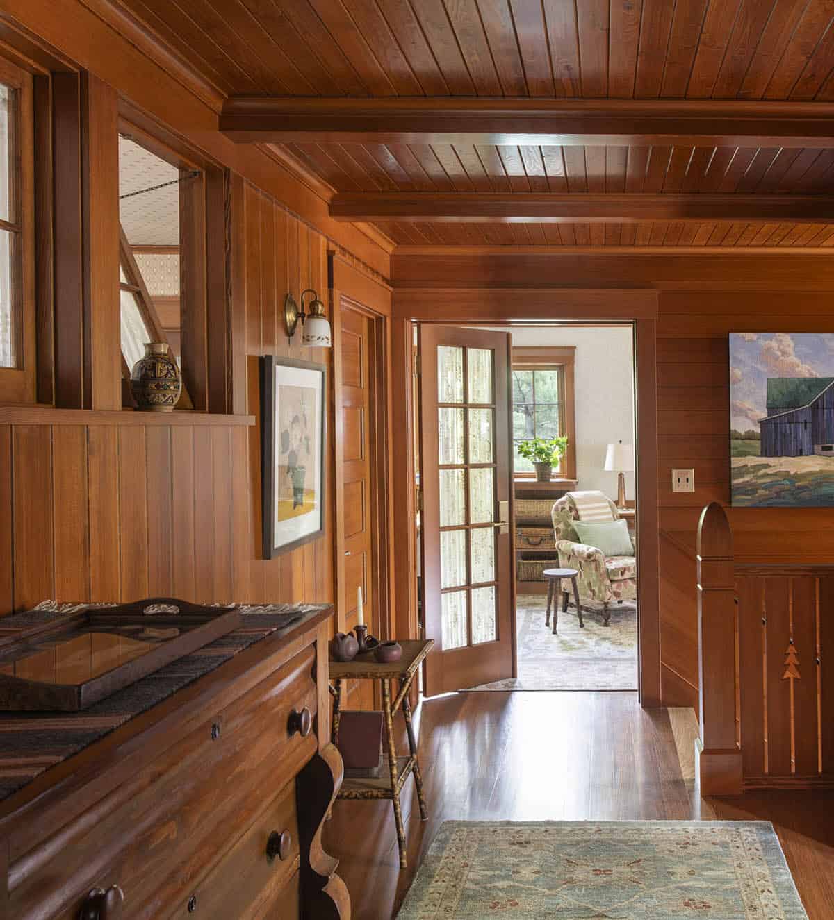 Upstairs hallway with warm cedar paneling, French doors, artwork, and hardwood floors