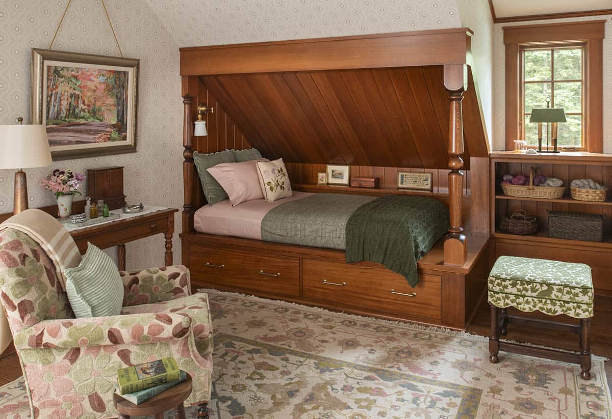 Attic bedroom with built-in cedar four-poster bed, under-bed storage drawers, and floral armchair