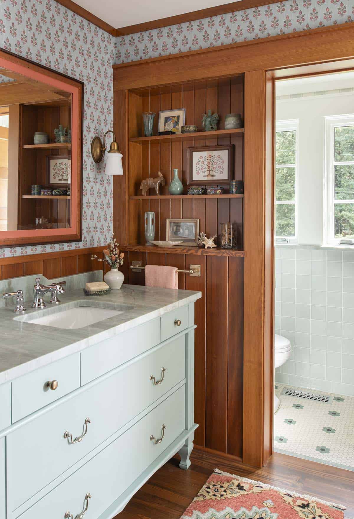 Bathroom vanity with mint green cabinetry, marble countertop, floral wallpaper, and built-in wood shelving