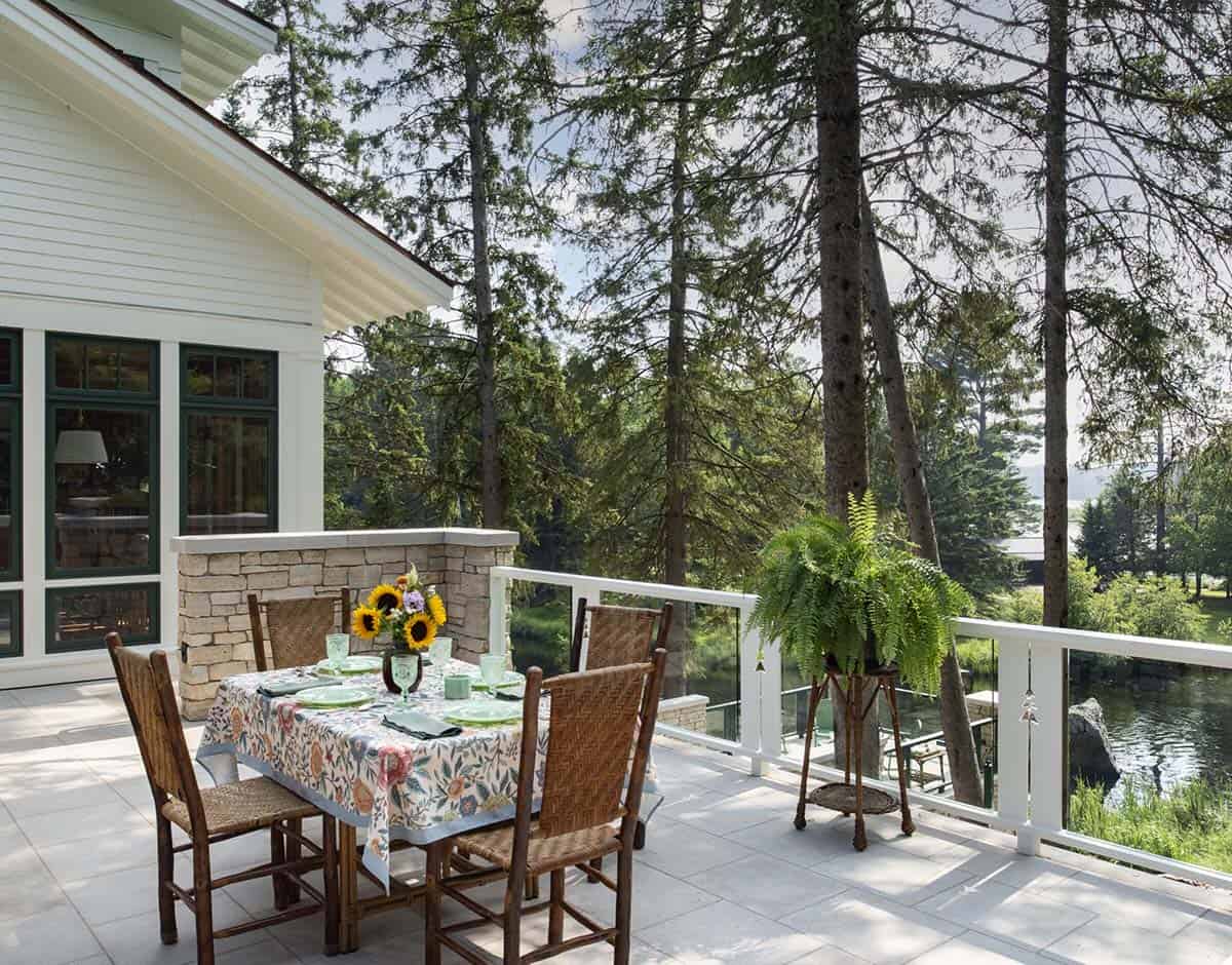 Outdoor dining table set with sunflowers on a stone terrace overlooking the lake through pine trees
