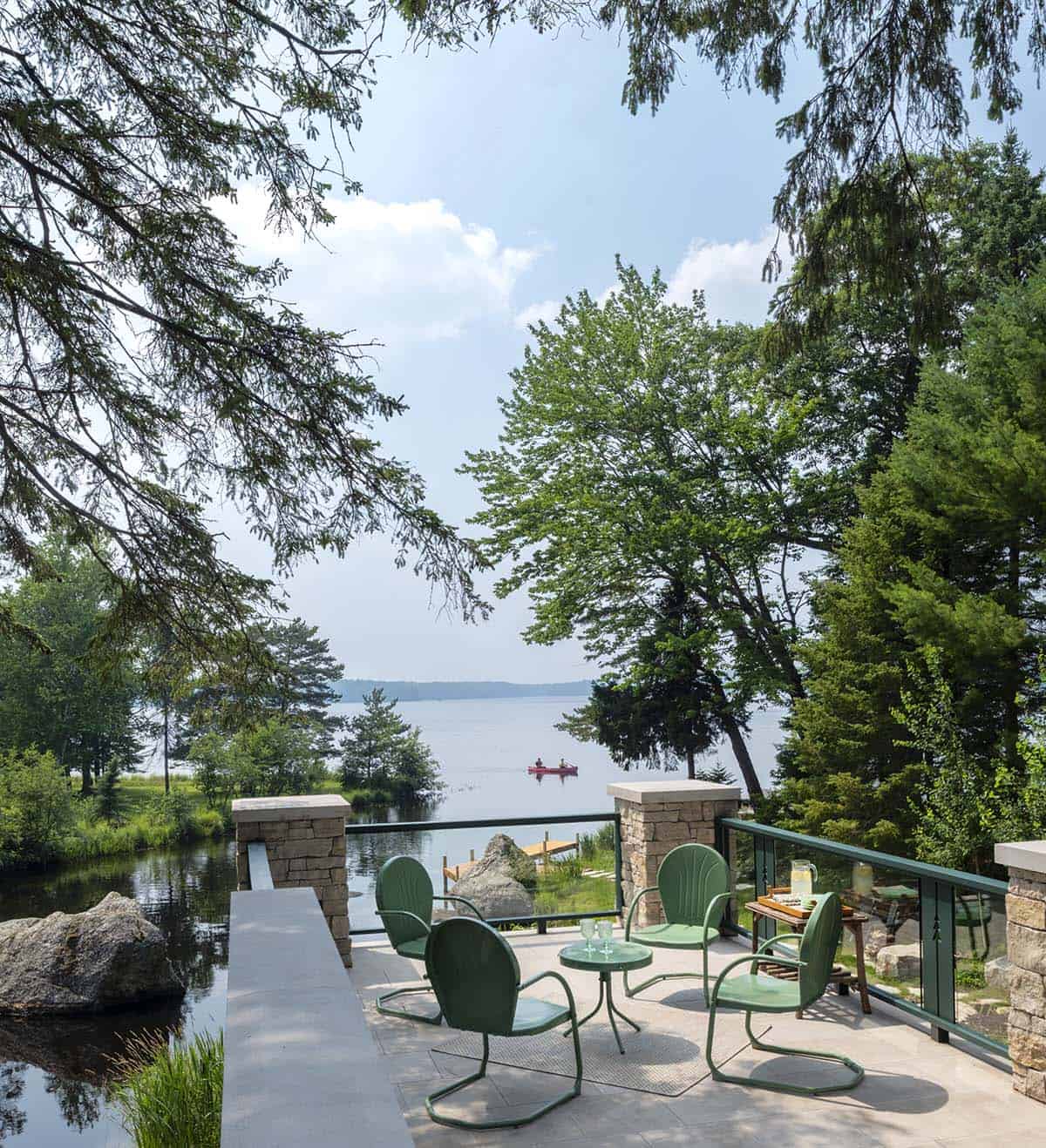Lower terrace with vintage green metal chairs overlooking a calm lake with a red canoe in the distance