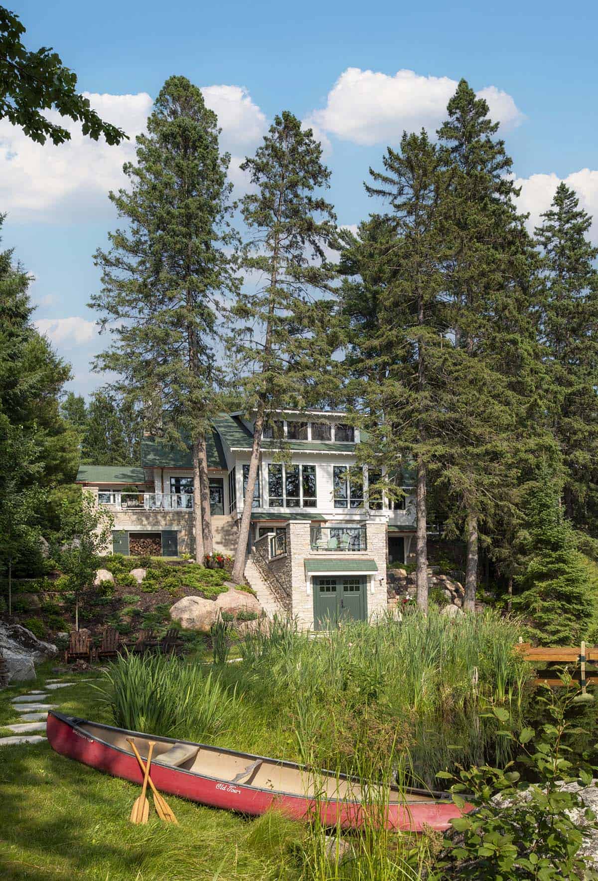 Full lakeside view of the cabin with red canoe in the foreground and pine trees framing the building
