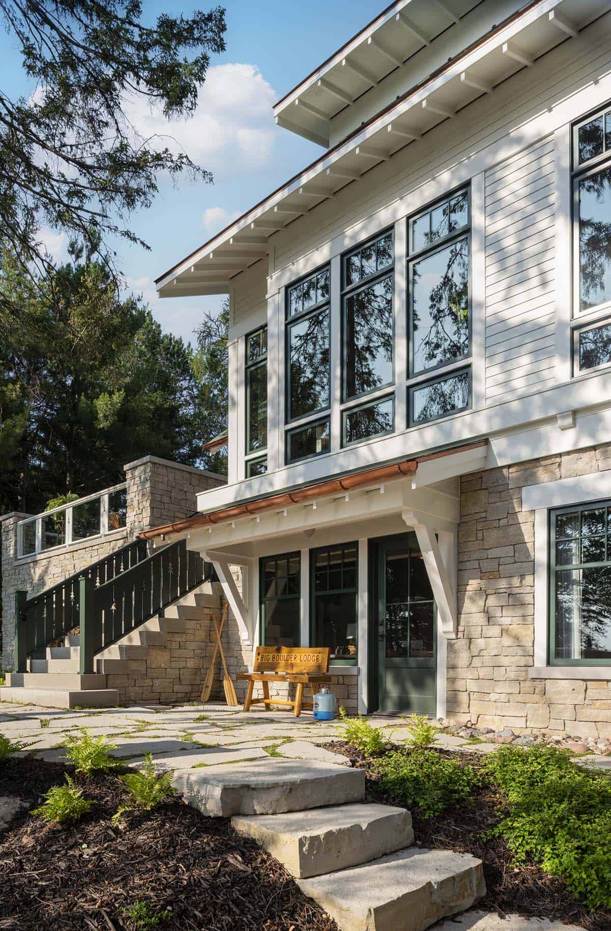 Lakeside entrance to the cabin with stone base, copper gutters, large windows, and stone steps