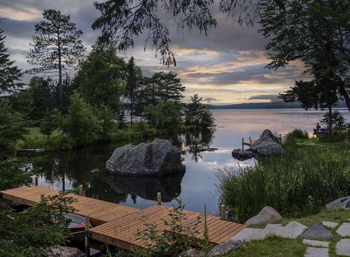 Wooden dock at sunset on a Wisconsin lake with large boulders, pine trees, and dramatic cloudy sky