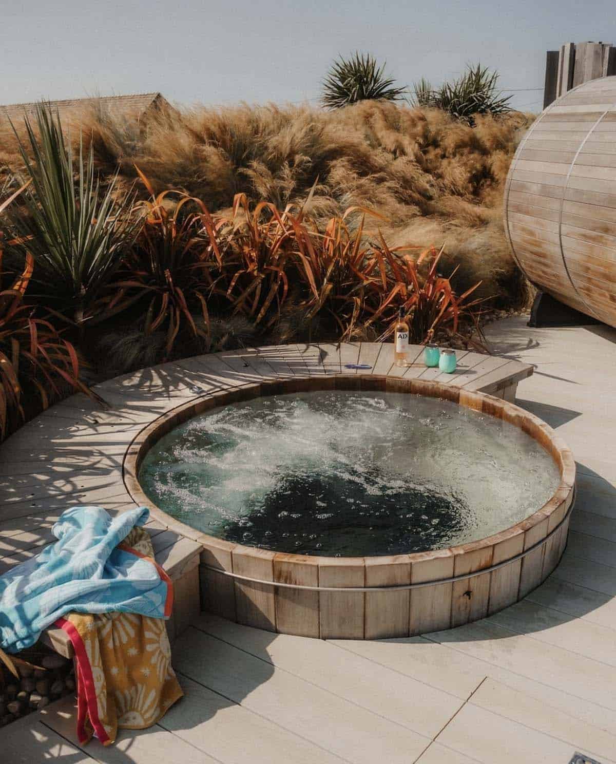 A round cedar hot tub set into a wraparound deck surrounded by coastal grasses in Cornwall