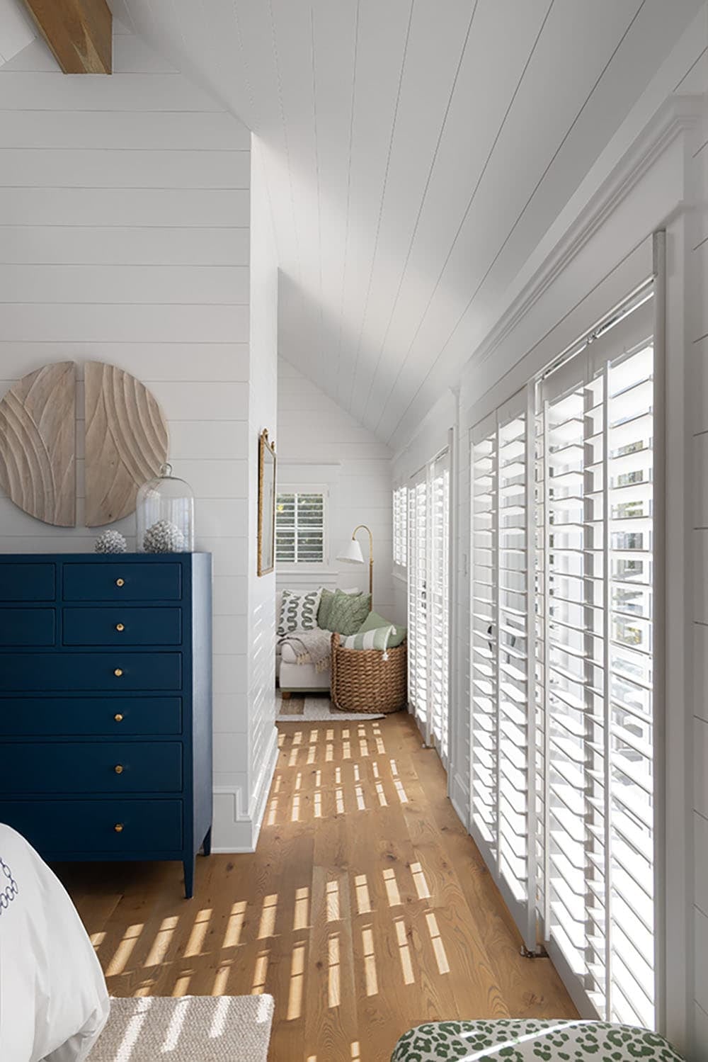 Hallway with shiplap walls, white plantation shutters, navy dresser, and a cozy reading nook with green and white pillows