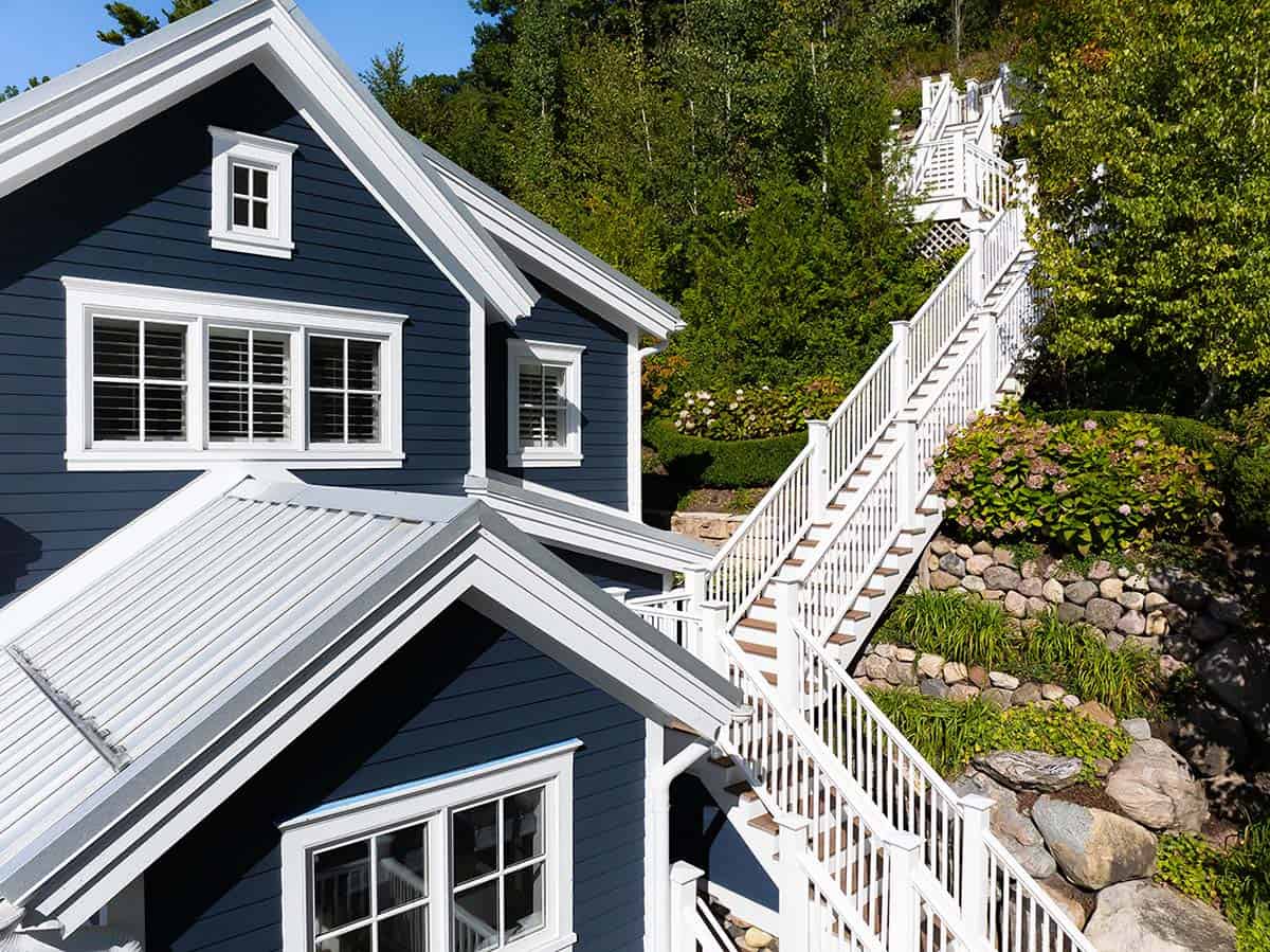 Close-up of navy blue house gables with white trim and a long staircase leading up the wooded hillside
