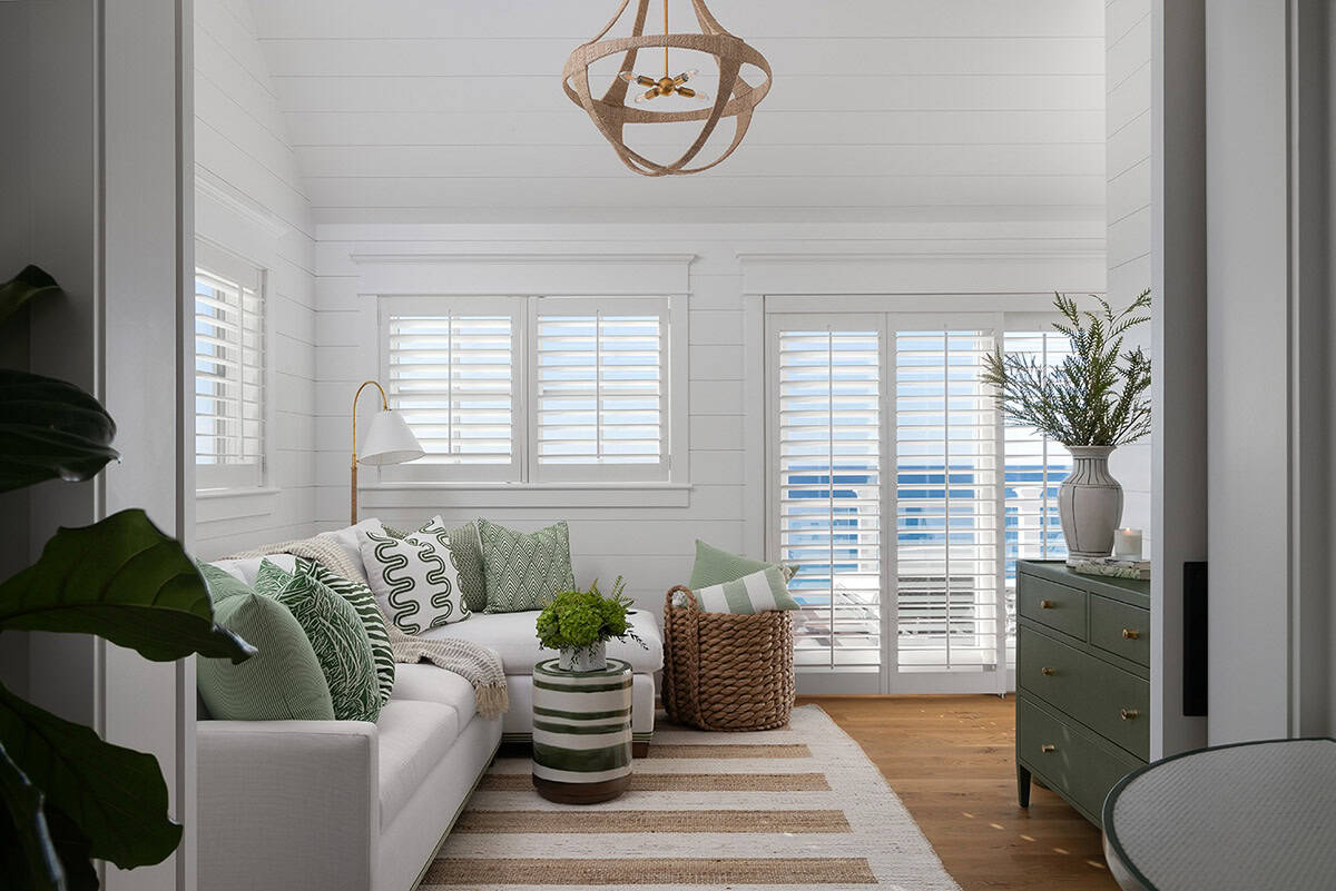 Cozy sitting room with white shiplap walls, green patterned pillows, woven basket, and plantation shutters