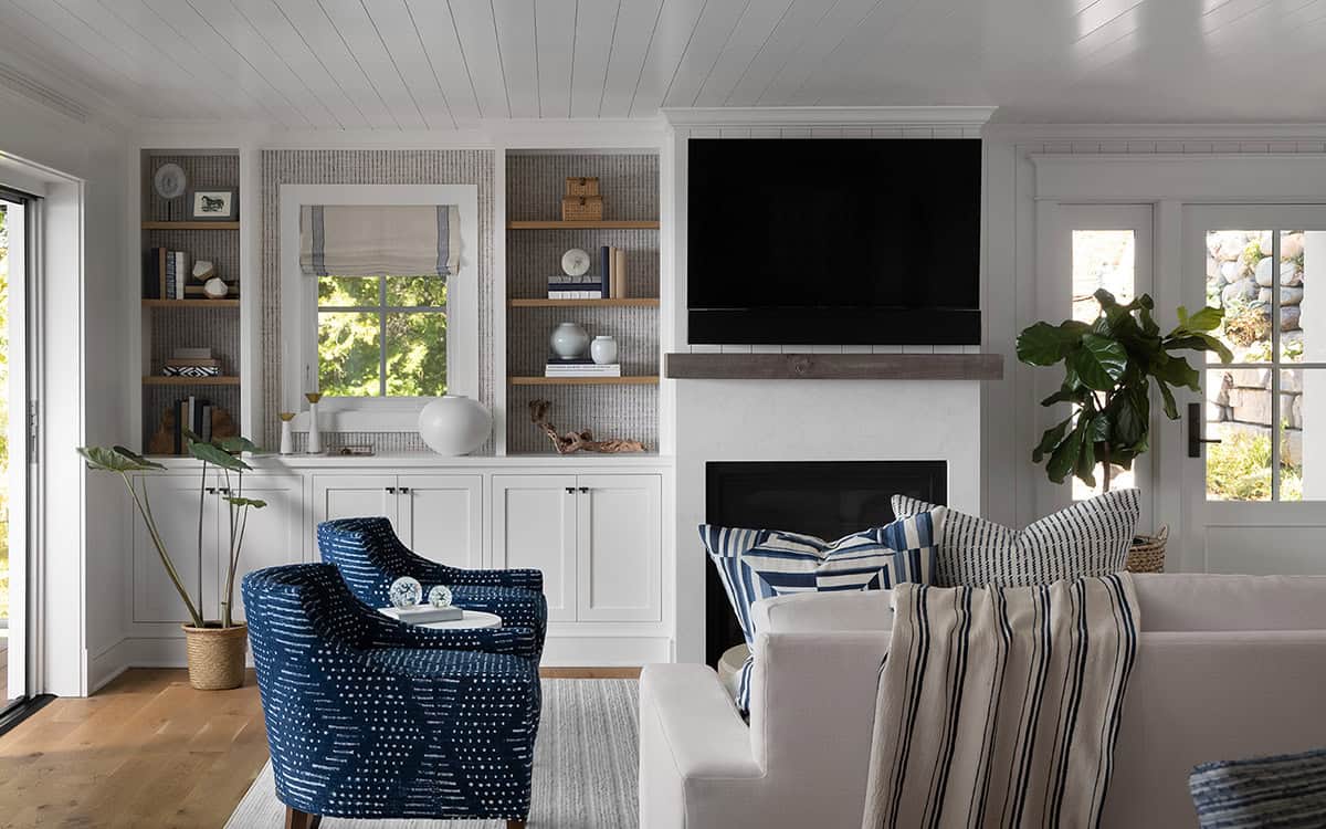 Living room with white built-in bookshelves, wall-mounted TV above a fireplace, and navy patterned armchairs