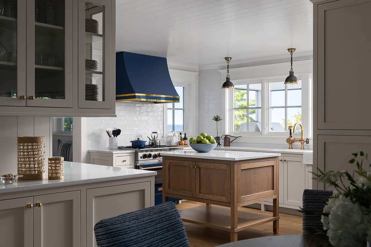 Kitchen with navy and gold range hood, white subtle cabinetry, wood island, and a bowl of green apples