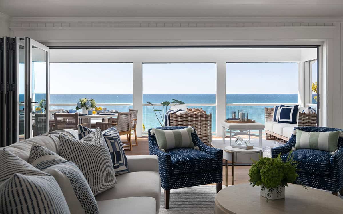 Living room with white sofa and navy patterned chairs opening onto a deck overlooking the lake