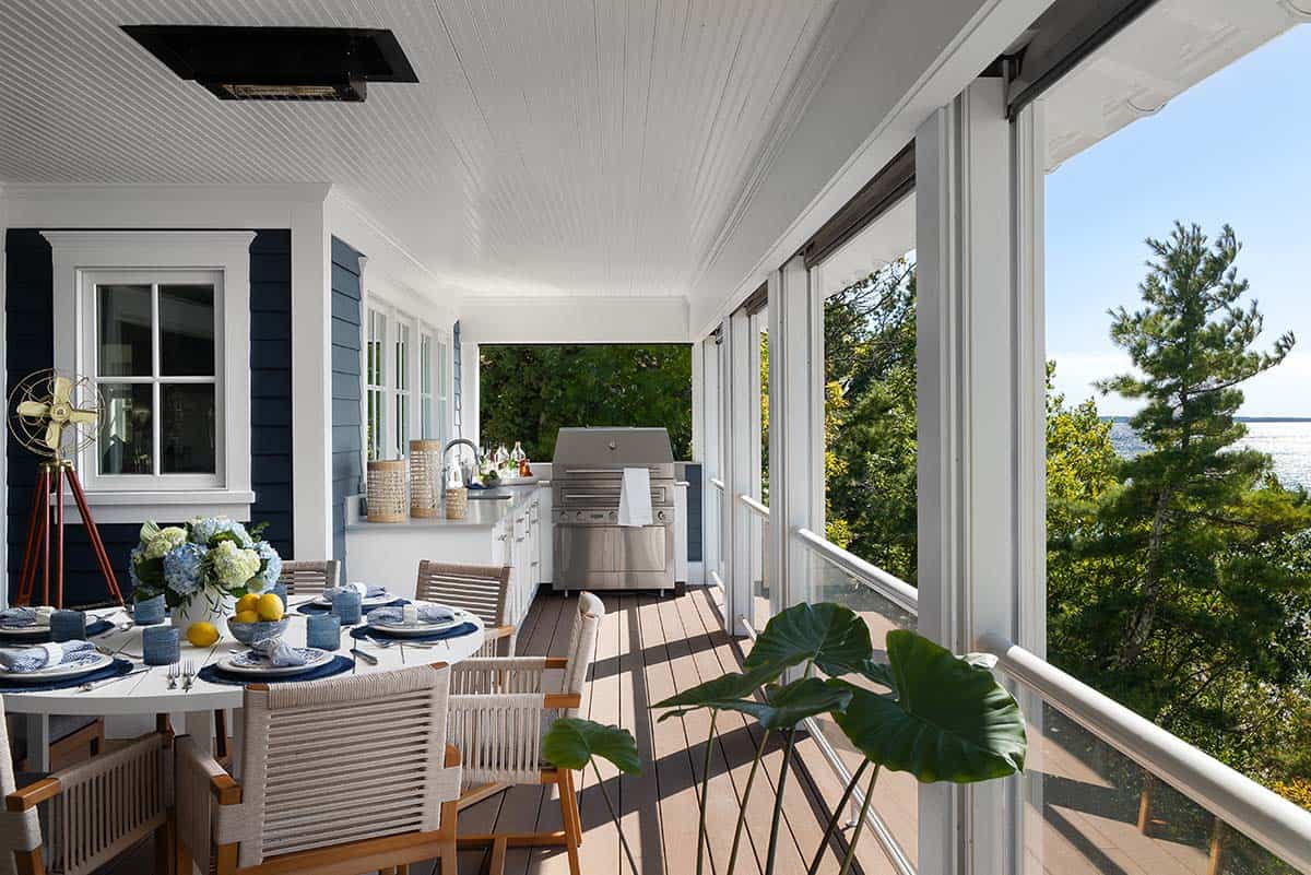 Screened porch with outdoor kitchen, dining table set with blue and white dishware, and a water view