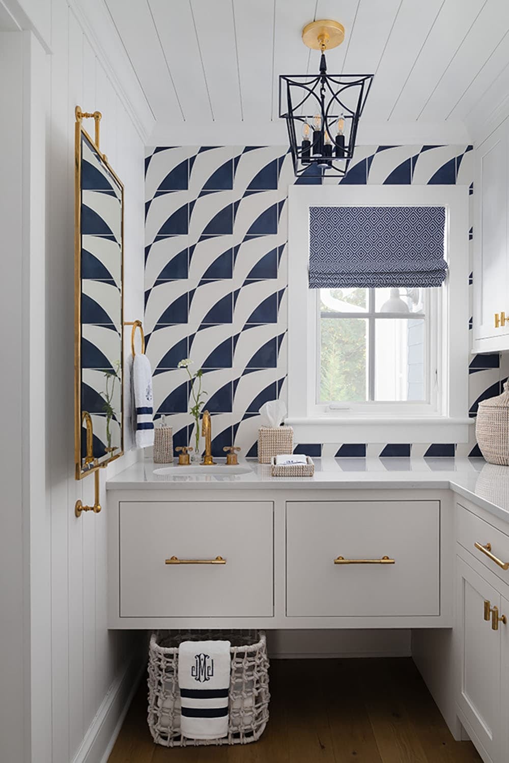Powder room with bold navy and white geometric tile, gold fixtures, black lantern pendant, and patterned roman shade