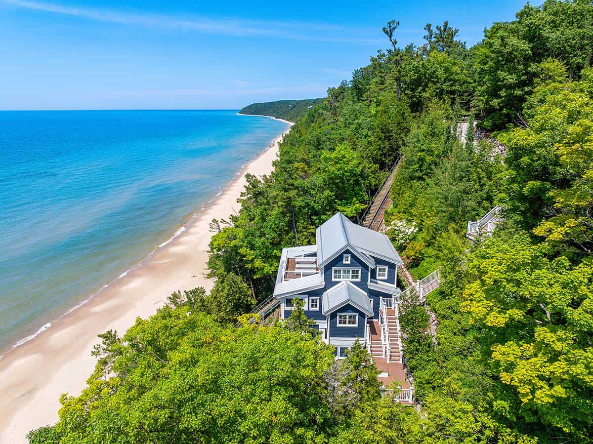 Aerial view of blue cliffside house with white staircase winding down through trees to the Lake Michigan shoreline