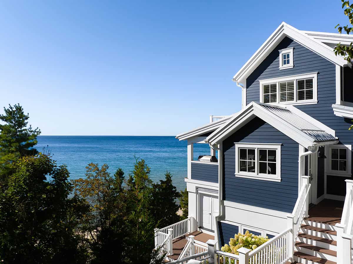 Close-up exterior of navy shingle-style house with white trim, decks, and stairs overlooking the lake
