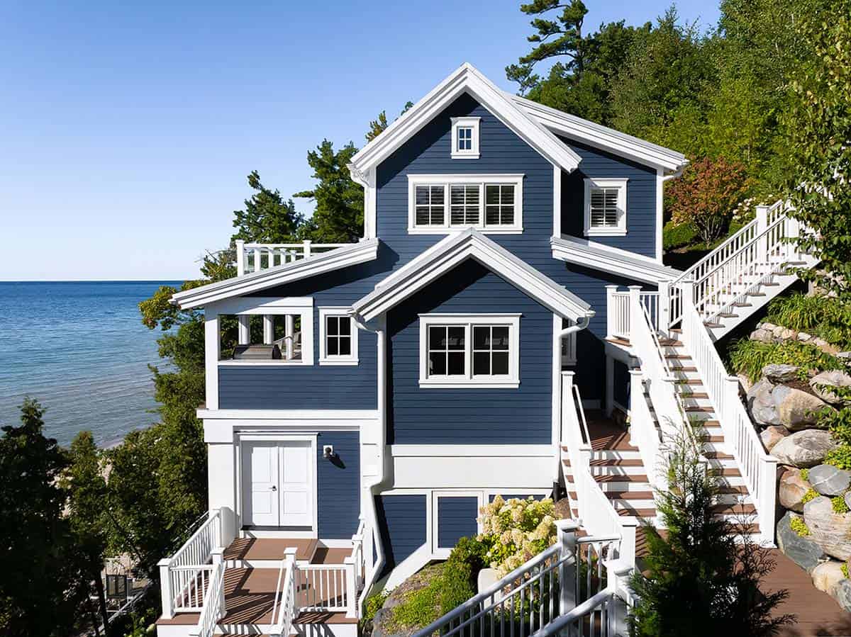 Three-story navy house with white trim, multiple gabled roofs, decks, and staircases set against the lake