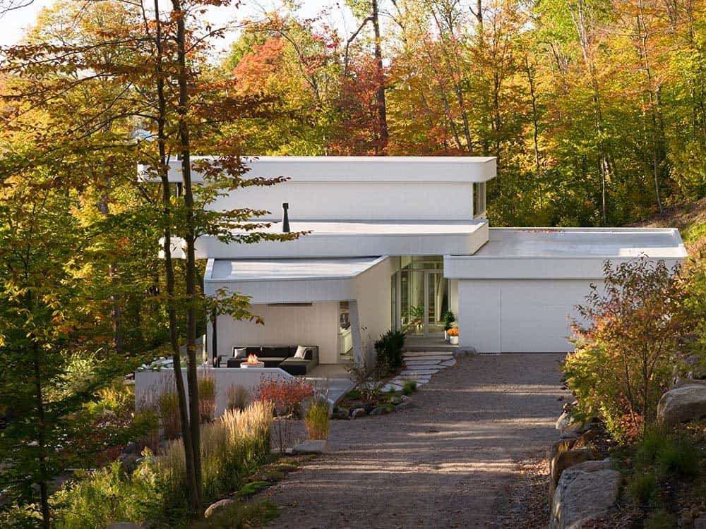 Contemporary white family home nestled among autumn trees with gravel driveway and outdoor seating area